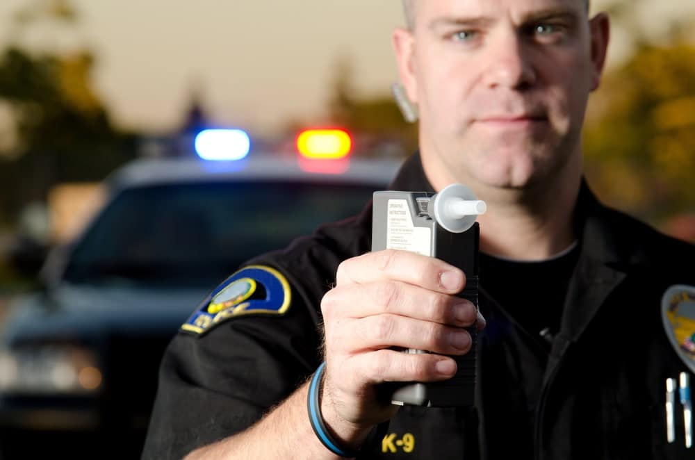 Image is of a police officer presenting a breathalyzer device, concept of roadside testing during a DUI in Florida stop.