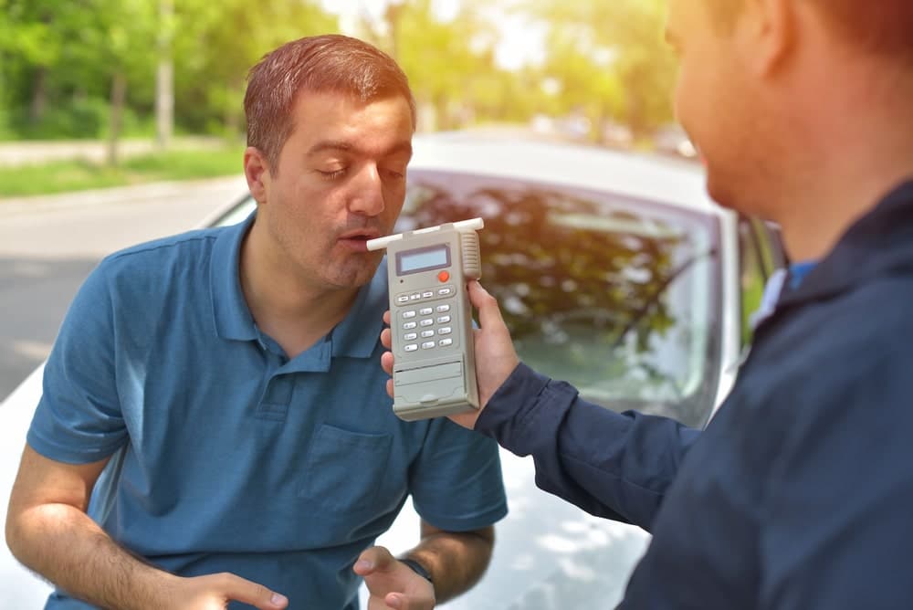 Image is of a driver blowing into a handheld device during a traffic stop, showing what happens when someone may refuse a breath test in Florida.