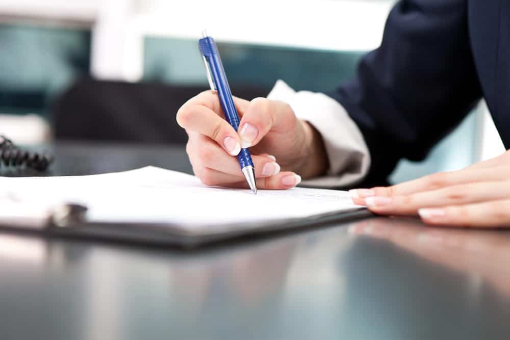 Image is of a person signing official paperwork on a desk, concept of expungement in Florida and completing administrative record clearance forms.