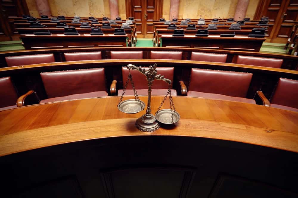 Image is of an empty courtroom with scales of justice displayed, highlighting the legal process that distinguishes administrative expungements from traditional court orders.