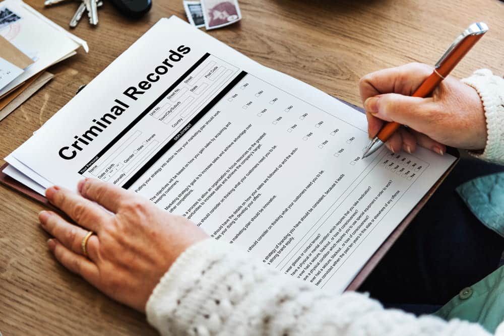Image is of a person reviewing and signing criminal record paperwork, illustrating how administrative expungements remove eligible records without a formal court order.