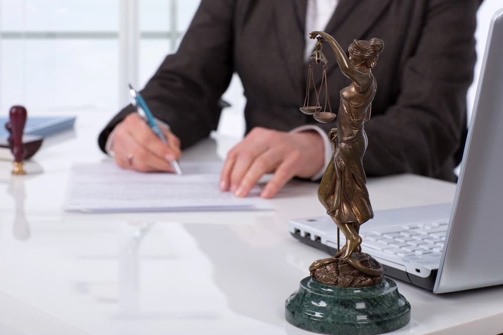 Image is of a lawyer reviewing paperwork beside a Lady Justice statue, symbolizing legal advocacy in human trafficking victim expungement