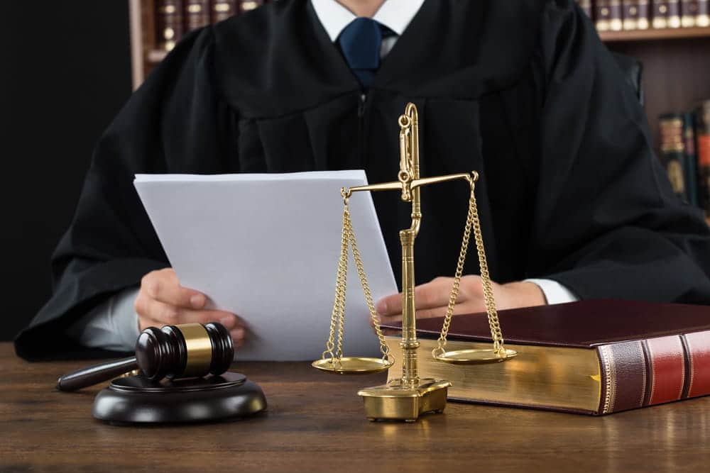 Image is of a judge holding documents with gavel and law books on desk, concept of stand your ground case court review