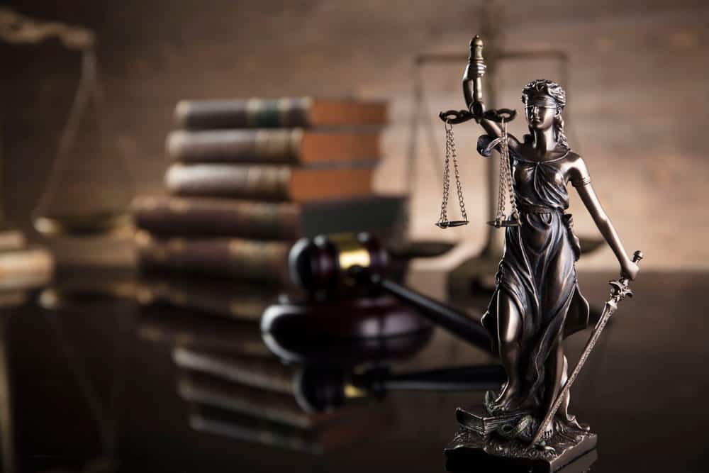 Image is of a Lady Justice statue with legal books and gavel in the background, concept of stand your ground case legal evaluation