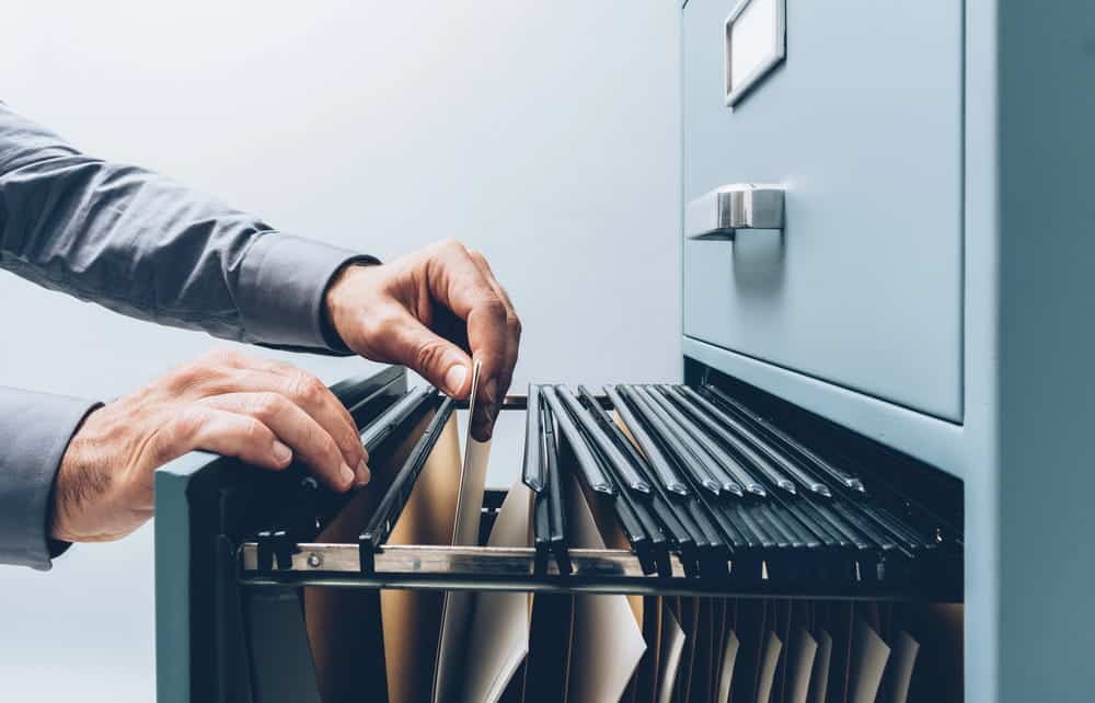 Image is of a person searching through a file cabinet containing legal records, concept of administrative expungement and reviewing criminal history files that may qualify for record removal.