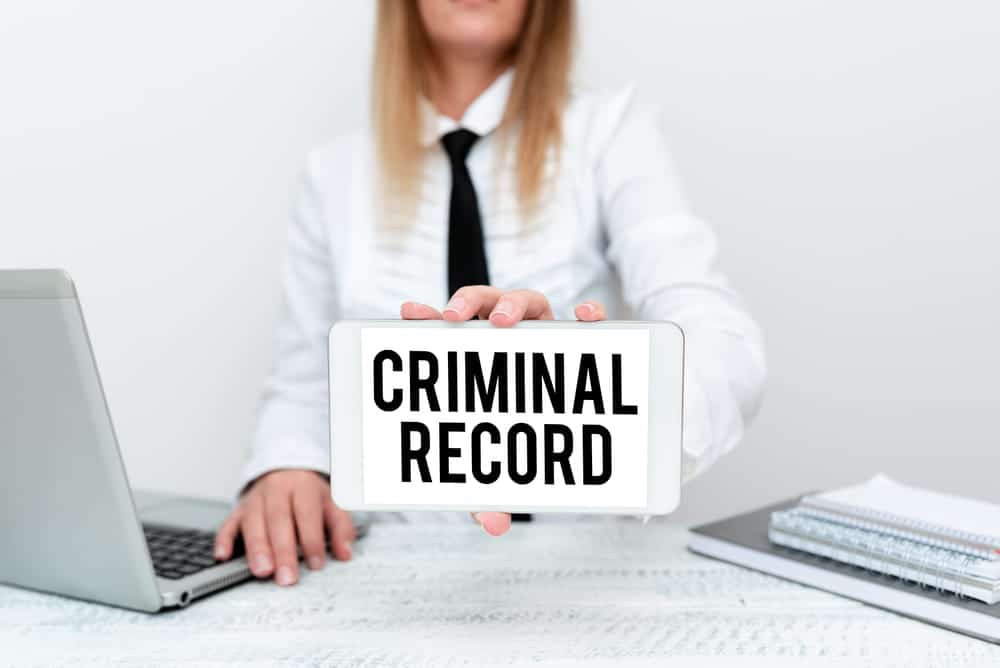 Image is of a professional holding a tablet displaying the words criminal record while working at a desk, concept of administrative expungement and removing incorrect records from a legal history.